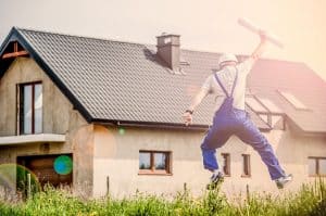 איש מקצוע עם קסדת בטיחות לבנייה קופץ בשמחה מול בית חדש